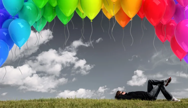 دراز کشیدن روی چمن با بادکنک های رنگی در آسمان