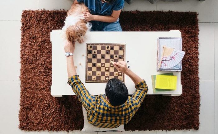 مرد و زن در حال بازی شطرنج در خانه روی میز با سگ
